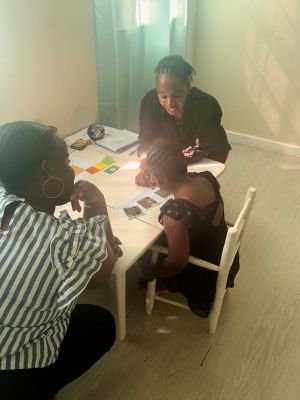 Image of speech and language therapist sitting at a table with a child looking at symbols. The child's mom is also stooping next to the table looking.